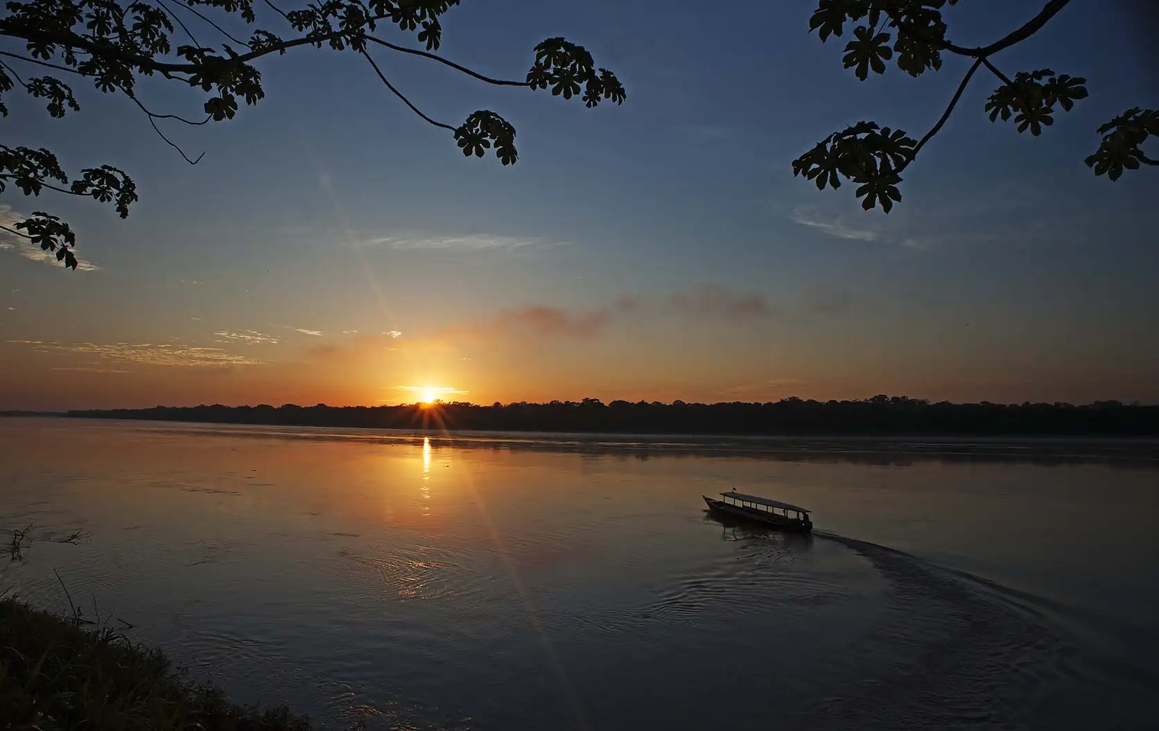 Sunset over a wide Amazonian river, with a boat crossing the water